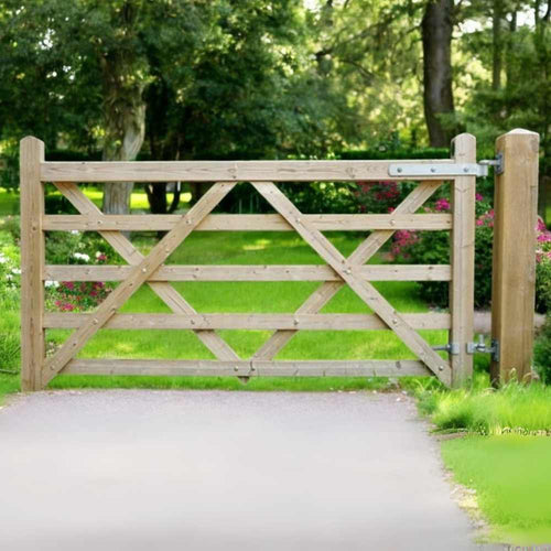 A Charlton Driveway/Field Gate 5 Bar, made from tanalised timber with a crisscross pattern, stands at the paths end. Its encircled by lush grass and colorful flowers. Tall trees can be seen in the sunny background.