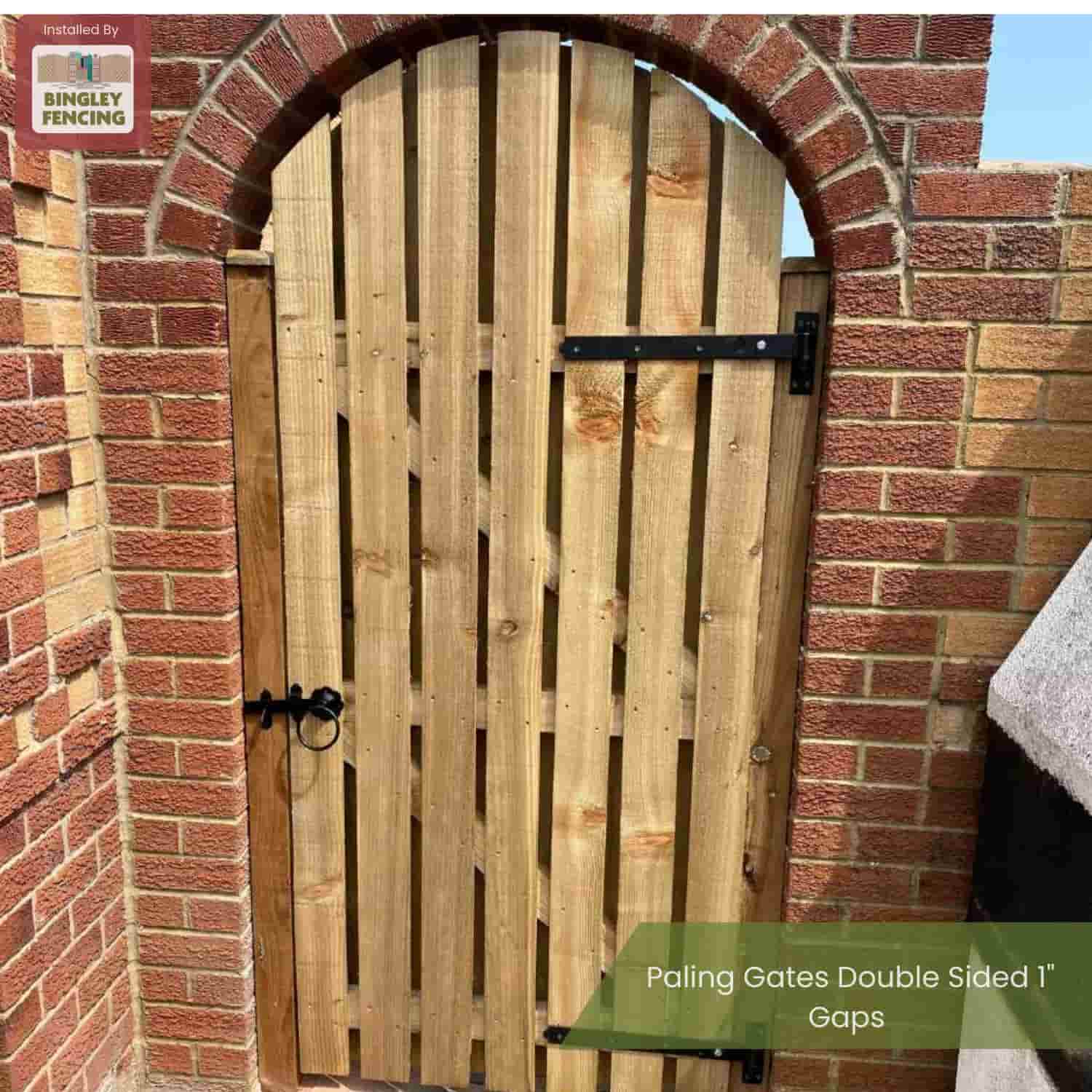 A Paling Gates Double Sided with 2" gaps (Flat Top & Arched Top) by Bingley Fencing is installed in a brick archway. The outdoor wooden gate features black metal hinges, a latch, and a small Bingley Fencing logo in the top left corner.