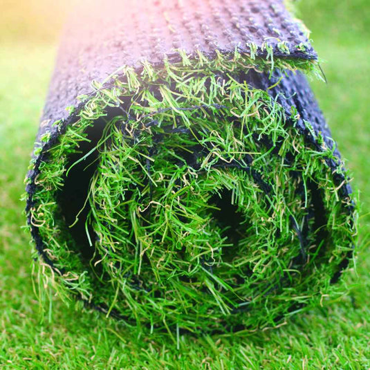 A roll of Bingley Fencing's Artificial Grass Supply & Fit is coiled tightly, featuring vibrant green blades with a textured black backing, resting on a grassy surface. Sunlight softly illuminates the top left corner of the image, highlighting our convenient next day delivery service.