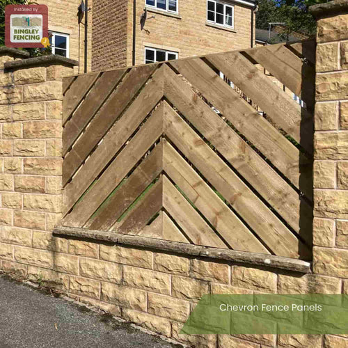A Chevron Fence Panel by Bingley Fencing, made from pressure-treated wood, stands between stone pillars atop a stone wall. A tan brick house is seen behind. Text: Chevron Fence Panels – Installed by Bingley Fencing.