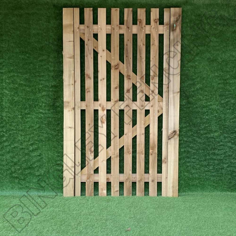Load image into Gallery viewer, A Bingley Fencing gate from the Paling Gates Single Sided collection, featuring 2" gaps in a vertical slat design with either a flat or arched top and supported by a diagonal beam, is showcased against a lush green grassy backdrop. Renowned for its low maintenance, this gate is equipped with a straightforward latch on one side.