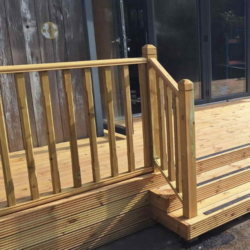 A newly built wooden deck with steps and a simple KDM Decking Handrail & Fillet (12' lengths, sold separately), featuring vertical smooth planed timber balusters. The deck adjoins a wooden building with large glass sliding doors.