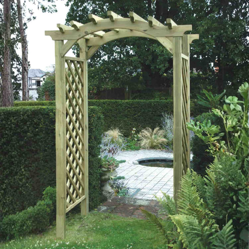 Constructed from tanalised softwood, the KDM Elite Omega Top Arch (EOTA2) features lattice sides and leads to a charming stone path bordered by greenery and trees under a cloudy sky. Enhance your outdoor space effortlessly with our expert installation service.