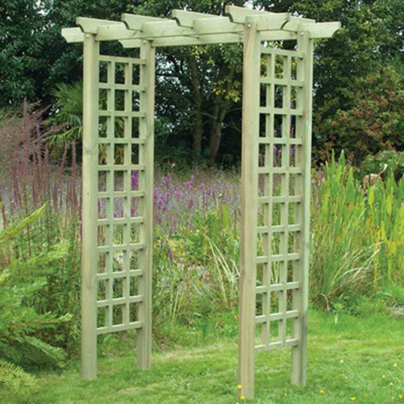 Load image into Gallery viewer, The KDM Reduced Flat Top Arch, crafted from tanalised softwood with a trellis design, is shown standing on a grassy lawn among green plants and wildflowers, with trees in the background.