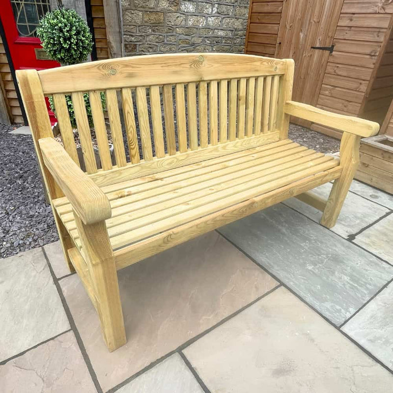 Load image into Gallery viewer, A light wood garden bench with slatted seat and backrest sits on a stone patio, next to a potted plant and a wooden shed.