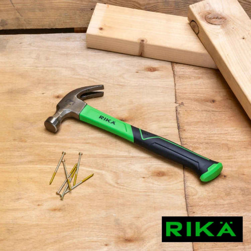 A RIKÄ 16oz Fibreglass Claw Hammer with Soft Grip in green and black rests on a wooden surface near several nails, wooden planks, and a 6mm tile drill bit, with the RIKA logo displayed in the bottom right corner.