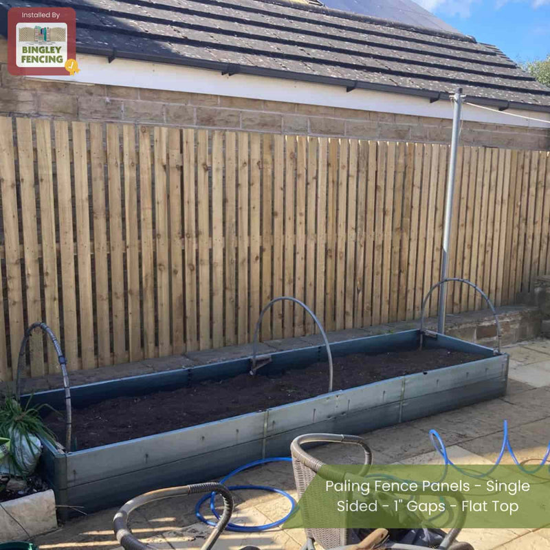 Load image into Gallery viewer, A Bingley Fencing Paling Fence Panel - Single Sided with 1 gaps and flat top stands behind a raised garden bed in a paved outdoor area. Metal hoops arch over the soil. Text overlay describes this fencing type.