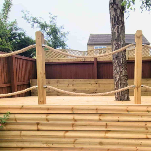 Featuring a raised wooden deck with Ironmonery Services 28mm Jute Decking Rope railing, a platform built around a tree, and timber fencing—ideal for West Yorkshire gardens. A house completes the scenic backdrop.