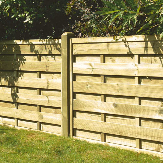 The KDM Square Horizontal Fence Panels (SH), made from pressure treated wood with a horizontal slat design and vertical posts, stand on a grassy lawn with trees and green foliage in the background.