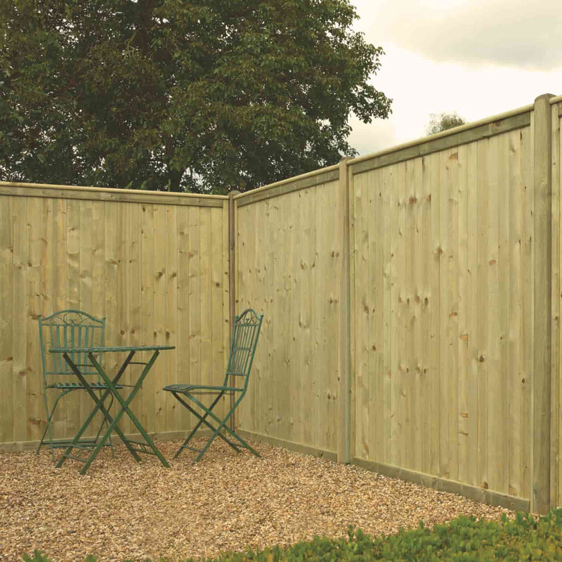 Load image into Gallery viewer, A compact outdoor seating area features a green metal table and two chairs on gravel, enclosed by tall KDM Tongue & Groove Fence Panels Flat Top (TGF), with a tree visible beyond the privacy fencing.