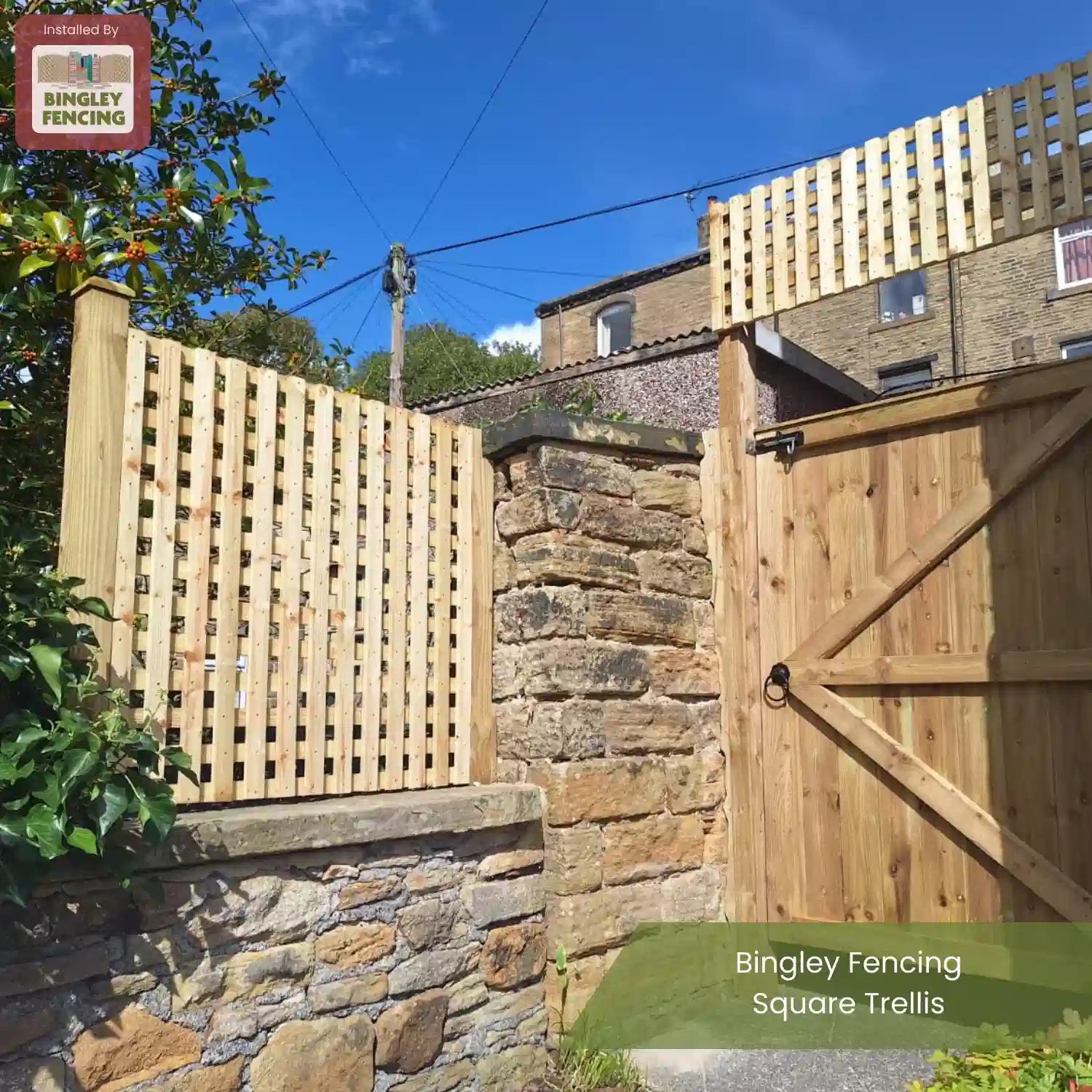 A wooden square trellis fence and gate by Bingley Fencing are installed on a stone wall in a sunny yard, with a clear blue sky and brick buildings in the background.