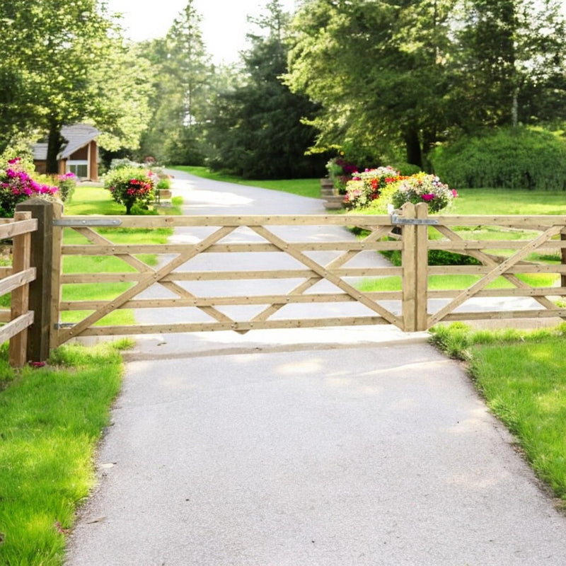 Load image into Gallery viewer, A Charlton Driveway/Field Gate 5 Bar, crafted from tanalised timber with a crisscross pattern, marks the entrance to a paved path. Colorful flowers in planters on either side enhance lush greenery and trees under a bright sky.