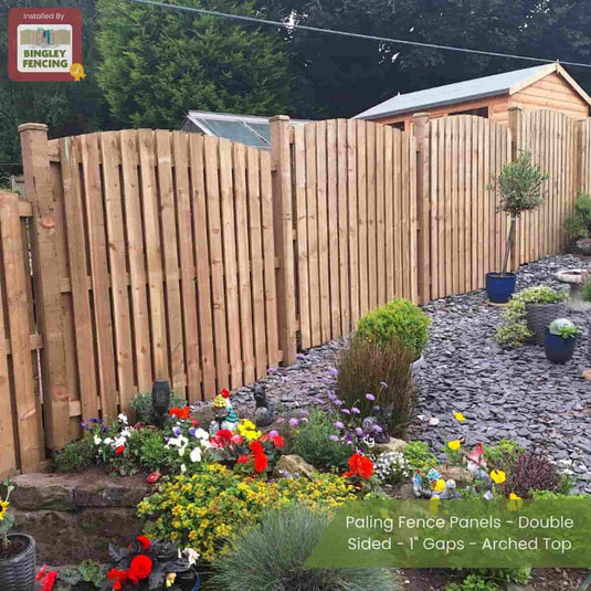 Bingley Fencing Paling Fence Panels - Double Sided with 1 gaps and arched tops separate a landscaped garden of colorful flowers and shrubs from a stone path, with a shed and green trees in the background.