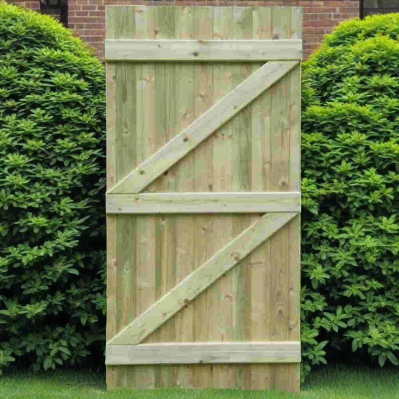 Load image into Gallery viewer, The Tongue & Groove (Flat) Euro-Gate by KDM, a tall wooden panel featuring diagonal cross bracing and a tongue & groove design, stands upright on the lawn, framed by lush green bushes. A brick wall in the background peeks through the foliage, enhancing the European gate aesthetic.