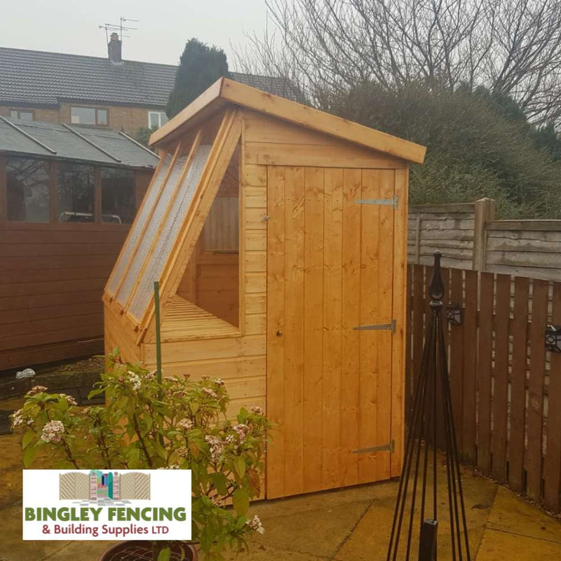Load image into Gallery viewer, In the backyard, a made-to-order Potting Shed from Bingley Fencing—Gardeners Choice—features a slanted, transparent roof. Visible fencing and bare trees surround it, with the Bingley Fencing logo in the corner.