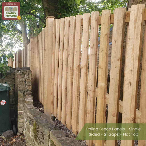 Bingley Fencing’s Double Sided Paling Fence Panels with 2 gaps and flat tops installed beside a stone wall in a leafy outdoor space. Green bin, dense trees visible; text overlay highlights installation details.