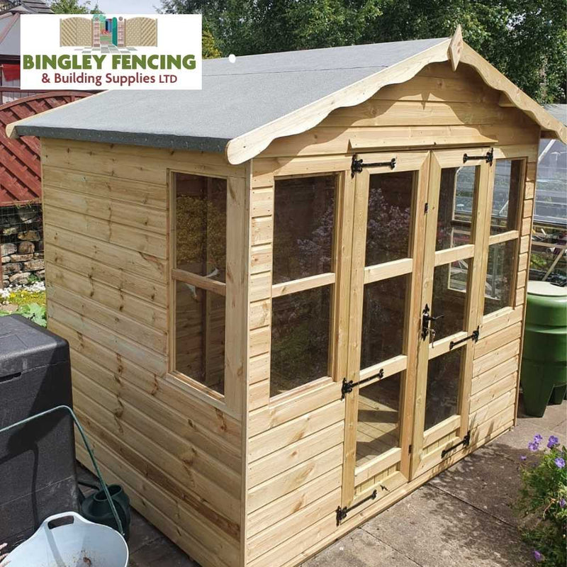 Load image into Gallery viewer, A Traditional Summerhouse crafted from wood, featuring glass windows and a gabled roof, is set on a concrete slab and surrounded by essential garden tools. This custom-designed structure proudly displays the Bingley Fencing logo in the top left corner.