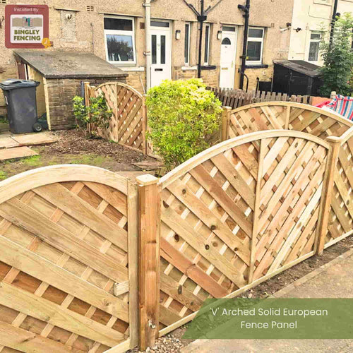 A garden bordered by KDM 'V' Arched Solid Fence Panel - VA forms a privacy fence between two houses, with a small shrub visible inside the fenced area.