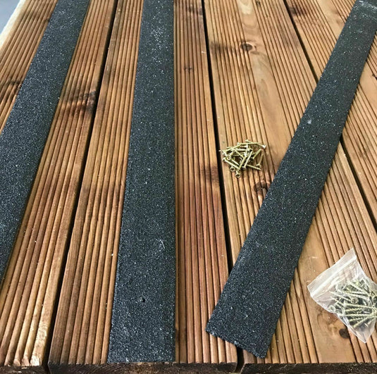 A set of Anti Slip Decking Strips 1200mm Long - Various Colours from Bingley Fencing, along with a small pile of screws in a plastic bag, are laid out on a wooden deck with visible grooves.