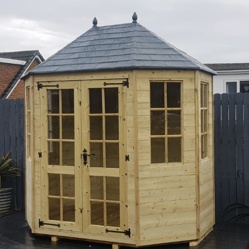Load image into Gallery viewer, A Bingley Fencing Octagonal Summerhouse showcasing an octagonal design and a gray pyramid-shaped roof, adorned with multiple glass-paneled doors and Georgian windows, is positioned on a patio with a wooden fence in the background. The sky is overcast.