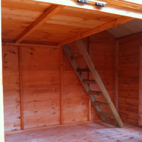 Load image into Gallery viewer, Interior view of the Adventure Kids Playhouse by Bingley Fencing, featuring orange-toned wood panels. A wooden ladder leads to a loft space above. This playhouse, crafted with child-friendly preservatives, is empty but showcases its simple and tidy construction.