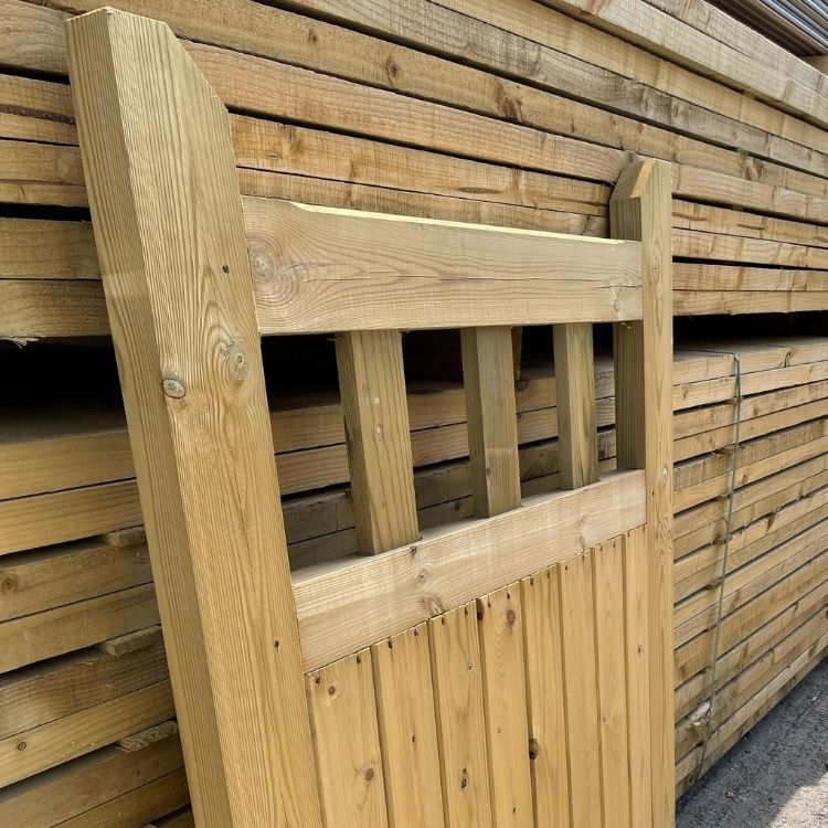 Load image into Gallery viewer, A KDM Regency Euro-Gate panel, with a design reminiscent of classic timber gates, is leaning gracefully against a stack of similar panels. The upper half showcases a slatted pattern, while the background displays an orderly arrangement of planks that echo the panel's charm and craftsmanship.