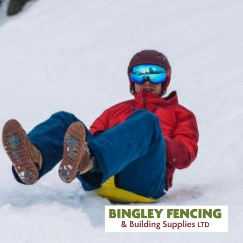 Load image into Gallery viewer, A person dressed in a red jacket and blue pants, with reflective goggles, is joyfully sledding down a snowy hill on our sturdy Hand Held Sledge – Blue Only. Their feet are playfully lifted in the air. The image features the Bingley Fencing logo in the corner.