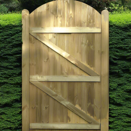 Load image into Gallery viewer, The KDM Tongue & Groove (Arched) Euro-Gate - TG180 features classic vertical planks and a diagonal Z-brace. Its natural wood finish stands out against a lush green hedge, providing style and privacy.