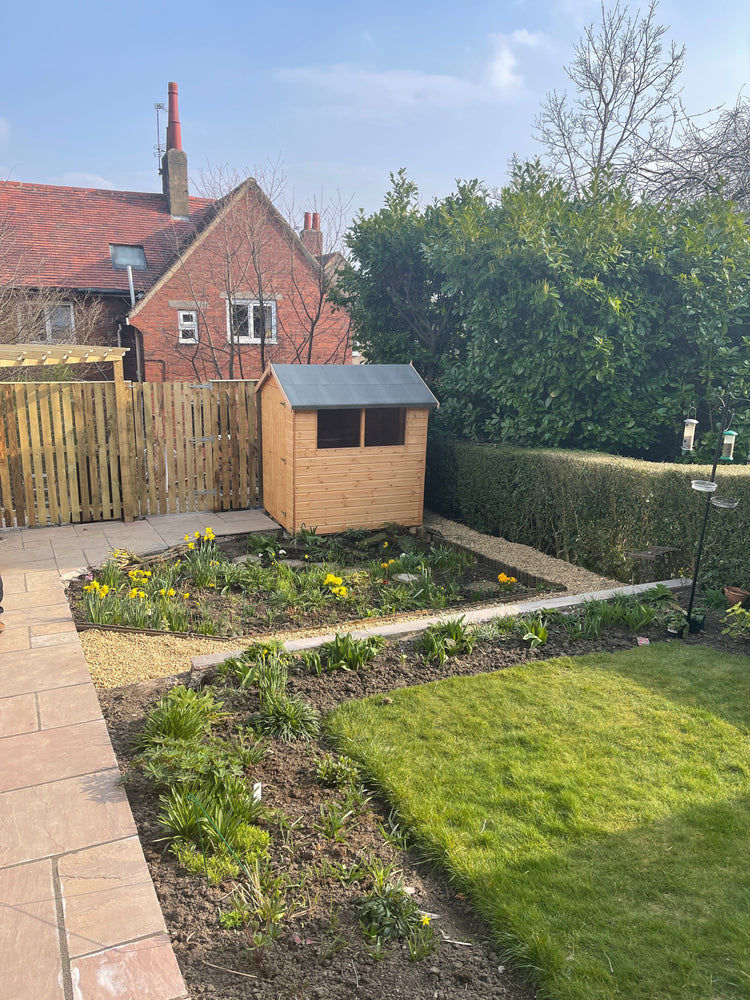 A small wooden garden shed installed at the corner of a customer garden