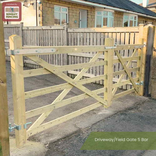 A Charlton Driveway/Field Gate 5 Bar, made from pressure treated timber, is installed at a home's entrance between wooden fence panels, with the house and windows visible in the background.