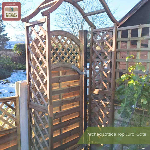A wooden arched lattice top gate is open, connecting a garden fence with similar lattice panels. The ground is partly covered in frost and sunlight creates shadows on the wooden structure.