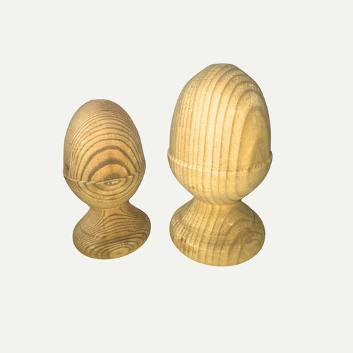 Two light-colored, egg-shaped wooden objects with visible grain patterns stand upright on round bases against a plain white background. These elegant KDM Acorn Finials, available in various sizes, serve as stylish fencing accessories to enhance the appearance of your fence posts.