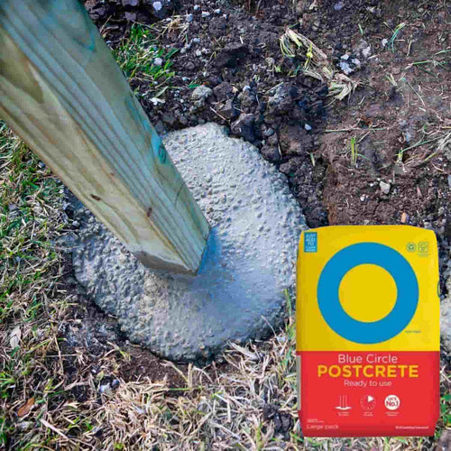 A wooden post set in fresh concrete in the ground, surrounded by grass and soil, with a Blue Circle - Post Mix 20kg Bag visible in the lower right corner.