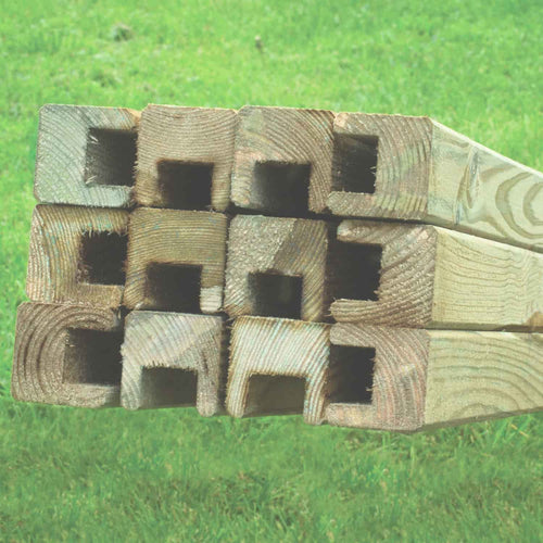 A close-up of KDM Fence Panel Repair Kit Framing: stacked timber posts with square holes, arranged horizontally on grass—perfect for repairing or assembling European fence panels.