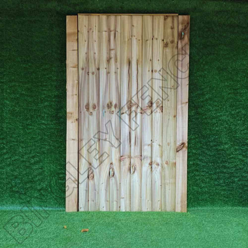 A wooden fence panel with vertical planks stands against a green backdrop, subtly displaying the words BINGLEY FENCING. Enhance your outdoor space with our Featheredge Gates available in Flat Top and Arched Top designs or explore our bespoke size gate options for seamless integration and style.