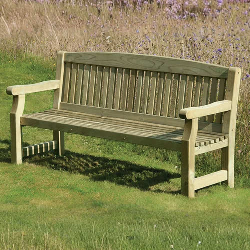 A wooden garden bench with armrests stands on green grass, surrounded by tall, dry grass and purple wildflowers in the background.
