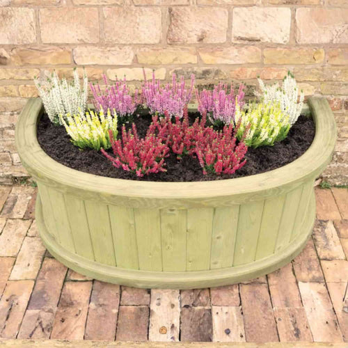 The KDM Half Moon Garden Planter - HMP, filled with dark soil and vibrant red, pink, and white flowers, sits elegantly on a brick patio by a stone wall—a top choice among West Yorkshire’s favorite garden planters.