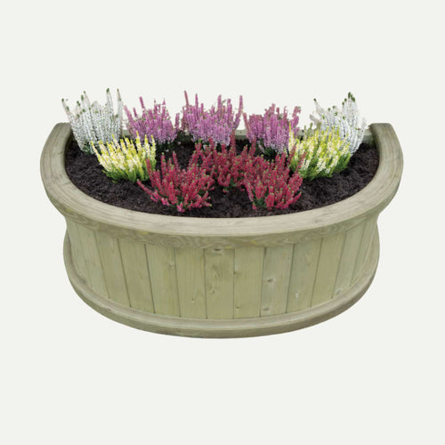 The KDM Half Moon Garden Planter - HMP, made from pressure-treated timber, overflows with rich soil and vibrant heather in white, pink, purple, and red, creating a charming display for your garden.