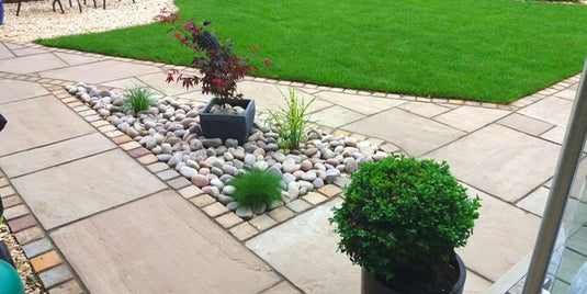 Grey paved patio area with pebbles and grass