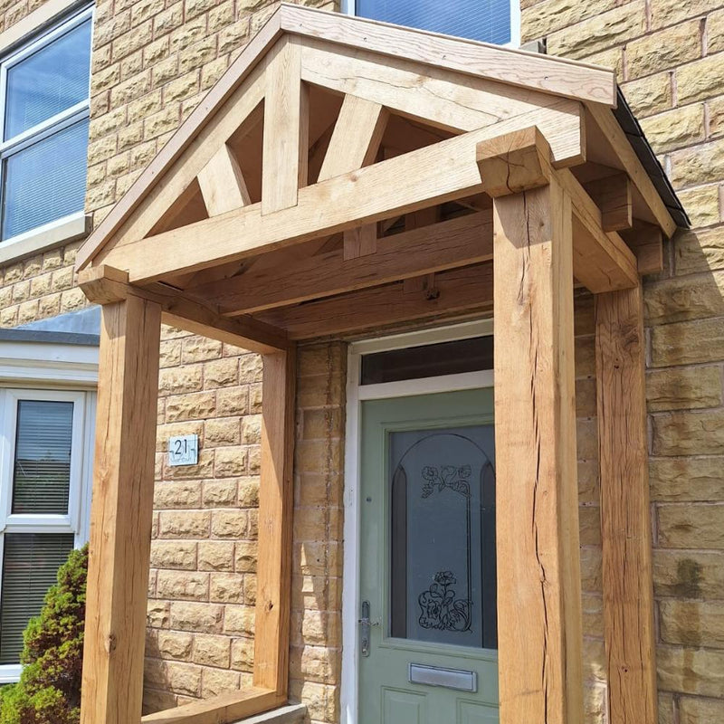 Load image into Gallery viewer, A brick house features a Bingley Fencing Traditional Oak Porch &amp; Frame with a triangular roof and exposed beams, sheltering a light green front door with decorative glass. The house number 21 is displayed beside the door.
