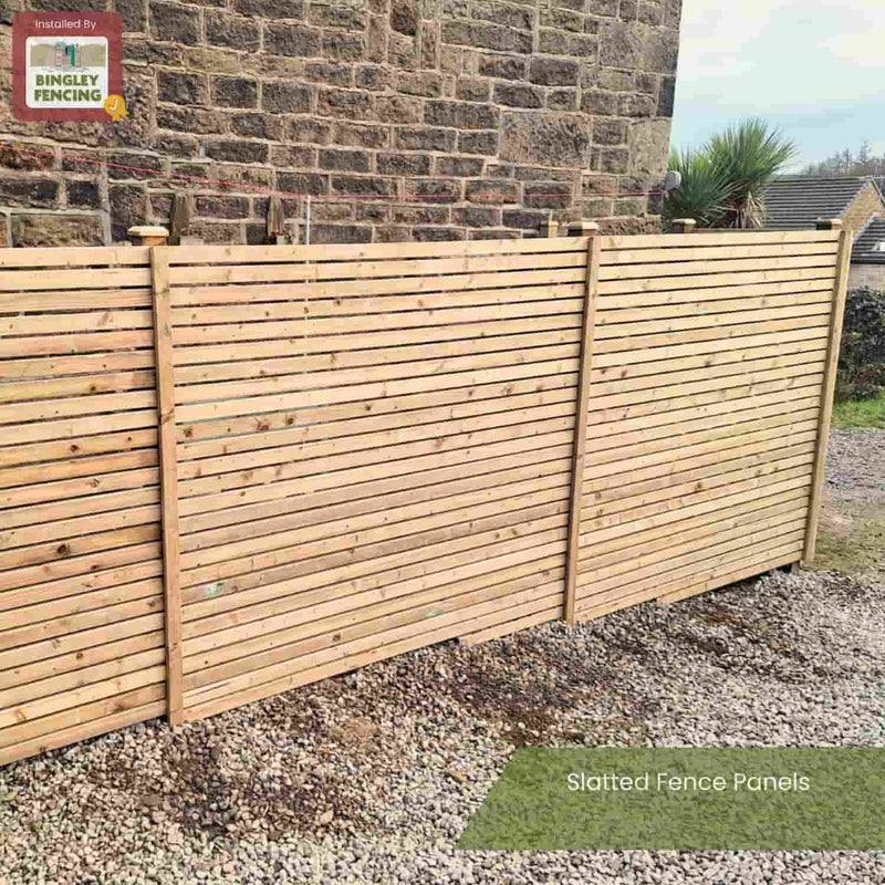 Load image into Gallery viewer, Three KDM Slatted Fence Panels with a contemporary wooden design are installed on gravel beside a brick wall, with plants and rooftops behind. The KDM logo appears in the top left corner, alongside the text Slatted Fence Panels.
