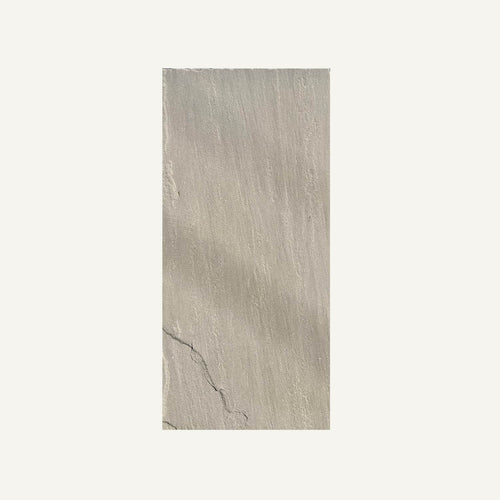 The Raj Green Indian Sandstone Paving Slabs by Bingley Fencing are light gray, rectangular, and feature a subtle linear texture with a faint diagonal crack—perfect for modern spaces and shown here against an off-white background.