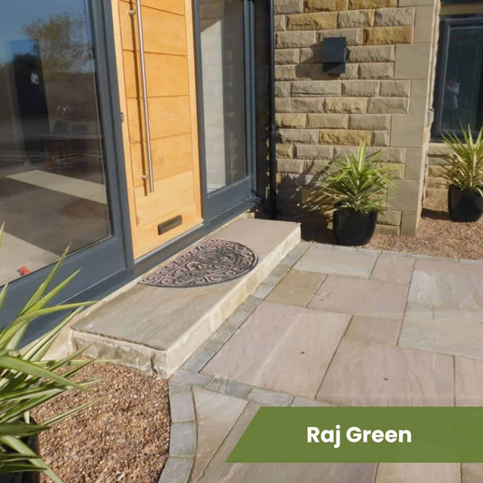 Front entrance with a light wooden door, stone step, patterned doormat, potted plants, stone wall, and tan-grey paving stones from the Bingley Fencing Indian Sandstone Paving Project Pack. Text overlay: Raj Green on a green banner.