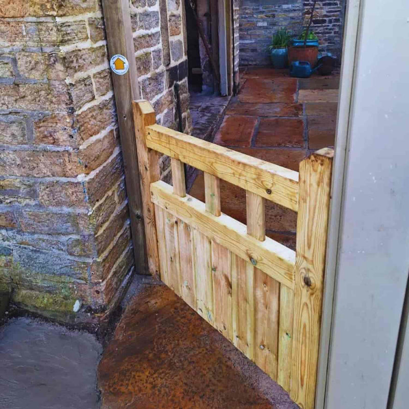 Load image into Gallery viewer, The KDM Regency Euro-Gate, a small timber gate with vertical slats, is installed between stone walls on a patio with reddish-brown tiles. Potted plants are seen in the background.
