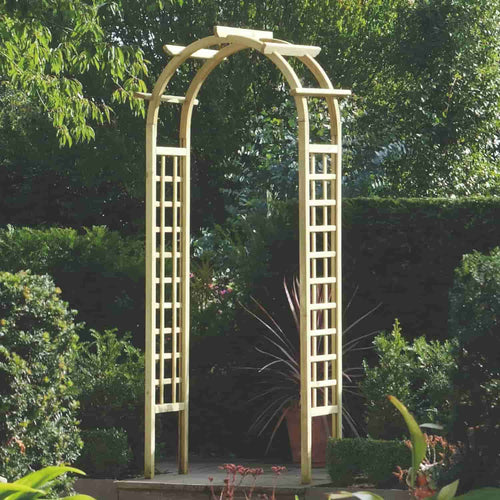 A KDM Rose Arch with lattice sides stands gracefully in a lush garden, serving as a charming feature. Encircled by an array of plants and shrubs, it creates a tranquil passage, while large potted plants enhance the foreground. This serene setting is ideal for those contemplating an installation service for their dream rose archway.