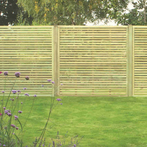 A modern garden features KDM Slatted Fence Panels made from pressure treated softwood. Purple flowers are in the foreground, with lush green trees rising behind the fencing for a stylish and private outdoor space.