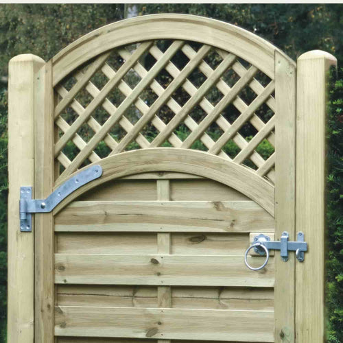 A wooden garden gate with an arched lattice top and horizontal planks below, fitted with metal hinges and a ring latch, is supported by KDM Smooth Planed European Gate Posts (3.5"x 3.5"). Green shrubbery shows behind the gate.