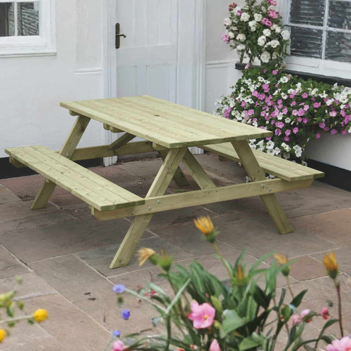 The KDM Standard A Frame Table 160cm x 180cm (SPB180) with benches is set on a stone patio near a white door, surrounded by blooming flowers—ideal for stylish outdoor dining.