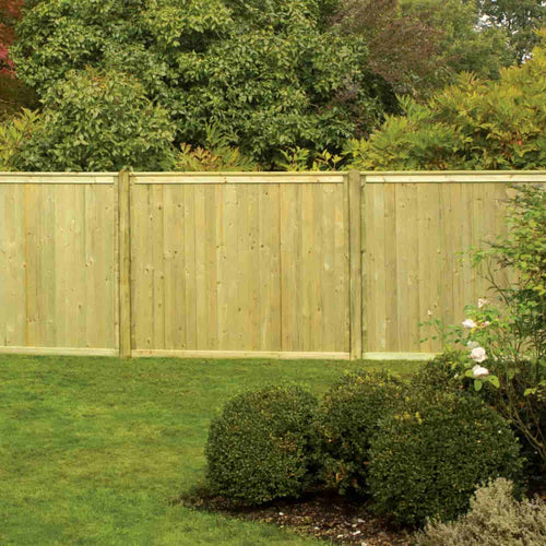 A KDM Tongue & Groove Fence Panels Flat Top (TGF) wooden privacy fence stands behind a neat lawn, with trimmed round shrubs and lush greenery in the background.