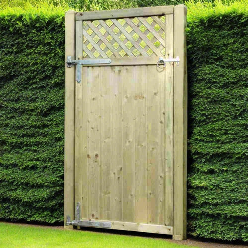 The Tongue & Groove Lattice Top Euro-Gate (TGLTG180) by KDM, set in a lush hedge with metal hinges and latch, elegantly complements the garden on a manicured lawn.